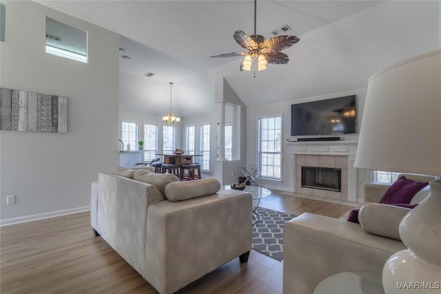 living room with hardwood / wood-style flooring, high vaulted ceiling, ceiling fan with notable chandelier, and a tile fireplace