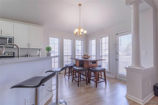 dining space featuring a notable chandelier, decorative columns, and light wood-type flooring