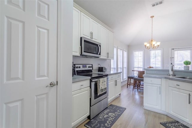 kitchen with appliances with stainless steel finishes, lofted ceiling, white cabinets, a chandelier, and light hardwood / wood-style flooring