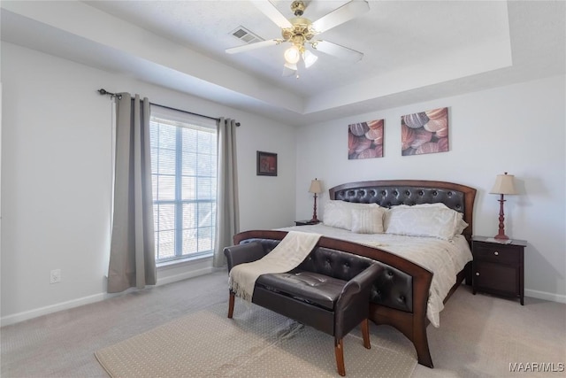 bedroom featuring ceiling fan, light colored carpet, a raised ceiling, and multiple windows