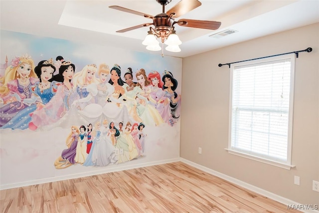 interior space featuring baseboards, visible vents, a ceiling fan, a raised ceiling, and wood finished floors