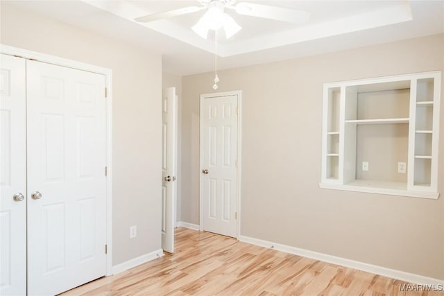 empty room featuring light wood-type flooring, baseboards, a raised ceiling, and a ceiling fan