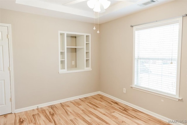 empty room with ceiling fan, a raised ceiling, and hardwood / wood-style floors