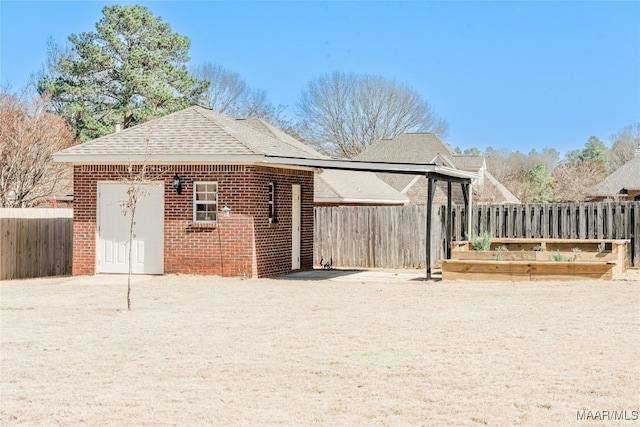 back of house featuring brick siding, roof with shingles, a fenced backyard, and a garden