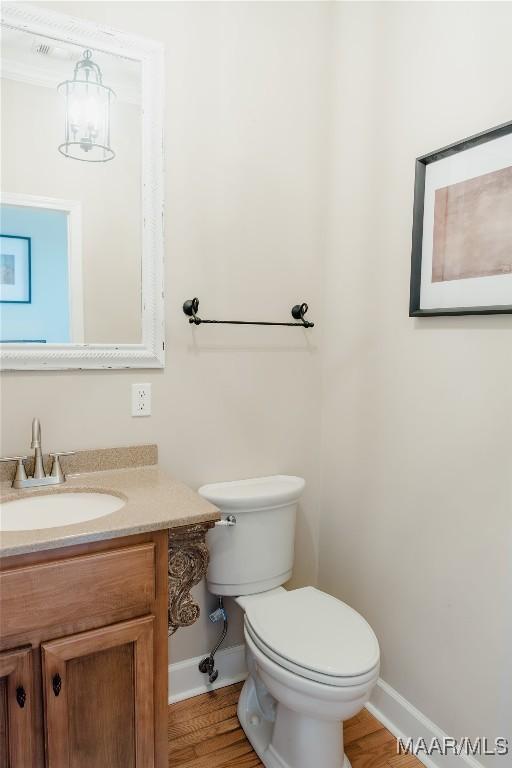 half bathroom with wood finished floors, vanity, toilet, and baseboards