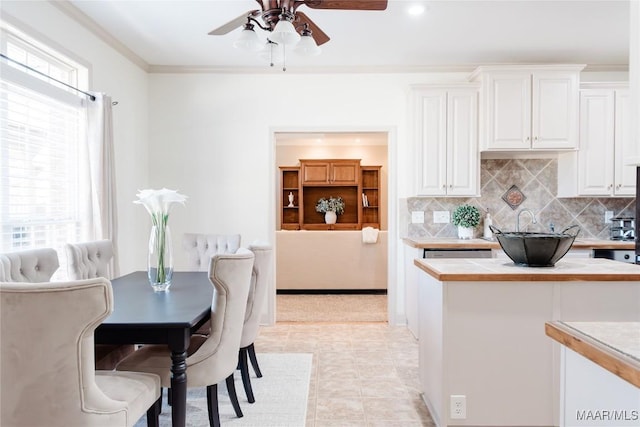 kitchen featuring tasteful backsplash, ceiling fan, crown molding, and white cabinets