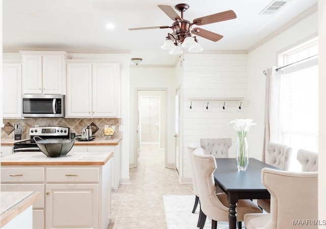 kitchen featuring appliances with stainless steel finishes, white cabinetry, decorative backsplash, ornamental molding, and ceiling fan