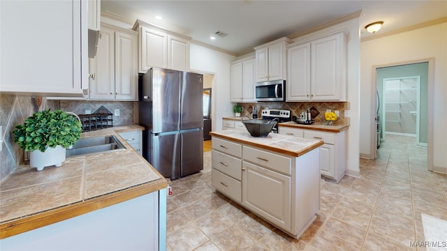 kitchen featuring crown molding, white cabinetry, backsplash, stainless steel appliances, and a center island