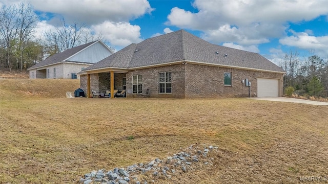 rear view of property featuring a garage, roof with shingles, a lawn, and brick siding