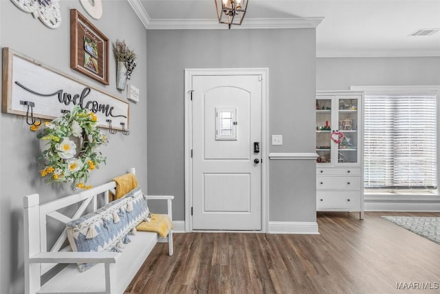 entryway featuring wood finished floors, visible vents, baseboards, ornamental molding, and an inviting chandelier