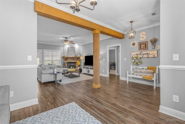 living room featuring ceiling fan with notable chandelier, dark wood finished floors, visible vents, and crown molding