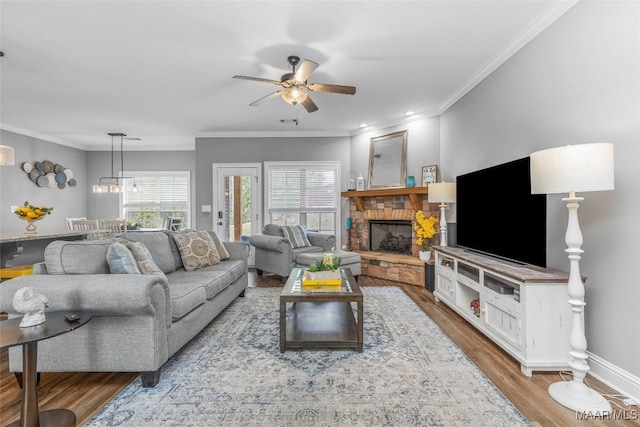 living area featuring baseboards, ceiling fan, ornamental molding, wood finished floors, and a fireplace