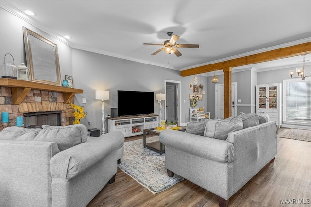 living room featuring ceiling fan with notable chandelier, crown molding, a stone fireplace, and wood finished floors