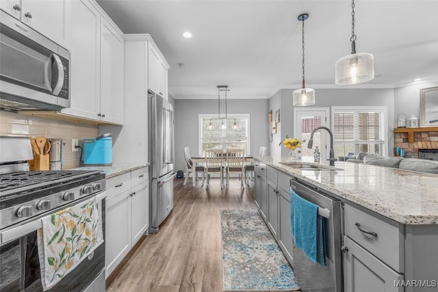 kitchen featuring decorative backsplash, appliances with stainless steel finishes, ornamental molding, a sink, and light wood-type flooring