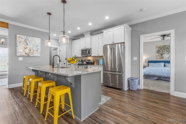 kitchen with appliances with stainless steel finishes, a kitchen island with sink, a sink, and dark wood-type flooring