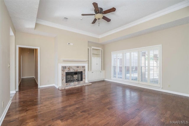 unfurnished living room with crown molding, dark wood-type flooring, a premium fireplace, ceiling fan, and built in shelves