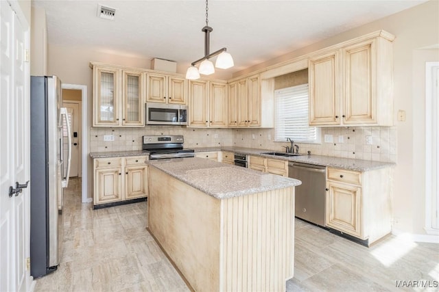 kitchen featuring sink, appliances with stainless steel finishes, a kitchen island, pendant lighting, and light stone countertops