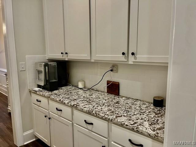 kitchen with white cabinetry, dark hardwood / wood-style flooring, light stone counters, and decorative backsplash