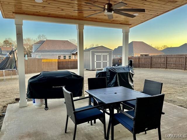 patio terrace at dusk with ceiling fan, a storage unit, area for grilling, and a trampoline