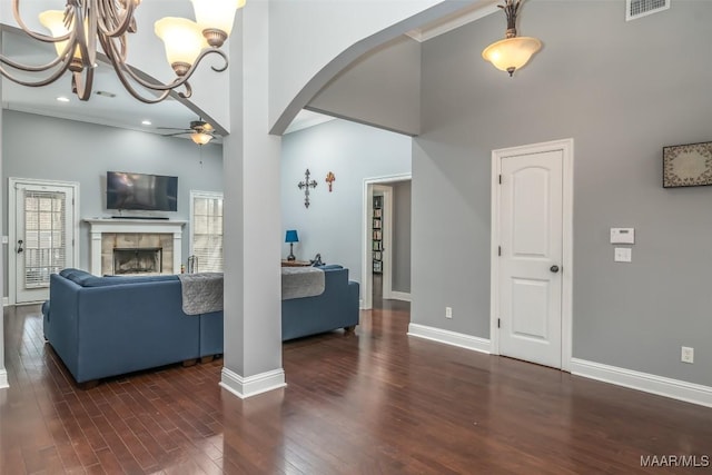 living room with a tiled fireplace, dark wood-type flooring, ceiling fan, and a towering ceiling