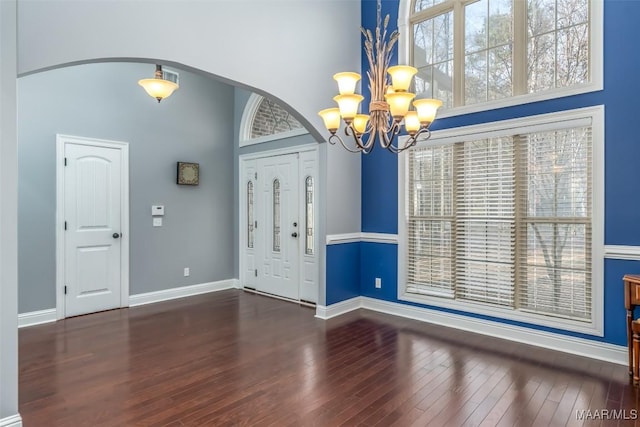 entryway with an inviting chandelier, a towering ceiling, and dark wood-type flooring