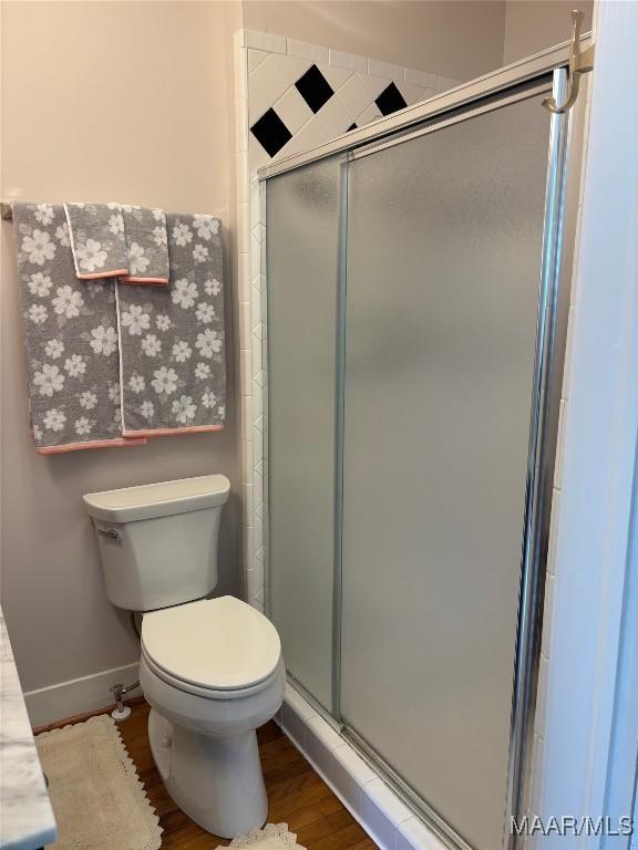 bathroom with hardwood / wood-style floors, an enclosed shower, and toilet