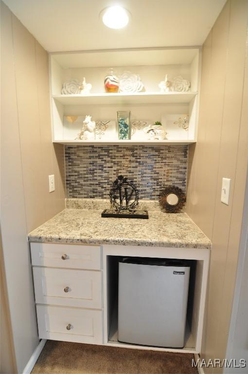 bar featuring light stone counters, white cabinetry, stainless steel fridge, and tasteful backsplash