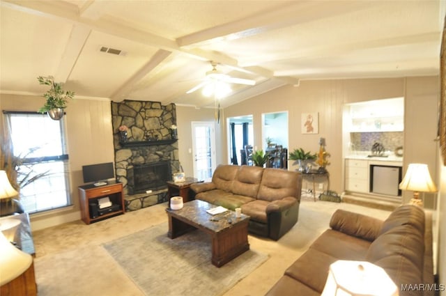 carpeted living room with a stone fireplace, a wealth of natural light, lofted ceiling with beams, and ceiling fan