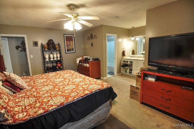 bedroom with ceiling fan, ensuite bath, light colored carpet, and a textured ceiling