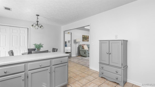 kitchen featuring pendant lighting, light tile patterned floors, gray cabinets, a textured ceiling, and a chandelier