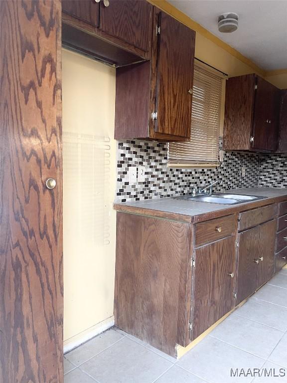 kitchen featuring dark brown cabinets, sink, light tile patterned floors, and decorative backsplash