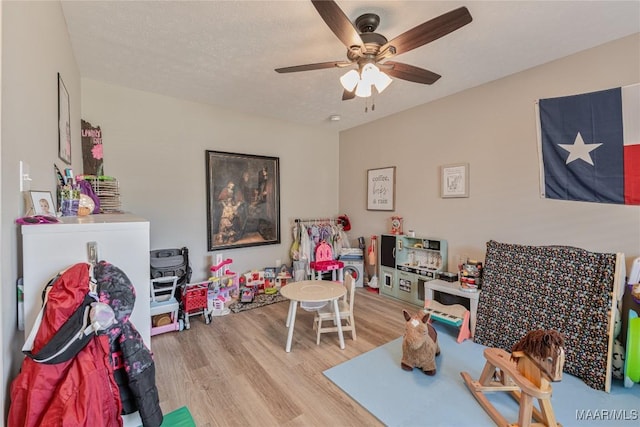 recreation room with ceiling fan, a textured ceiling, and light wood-type flooring