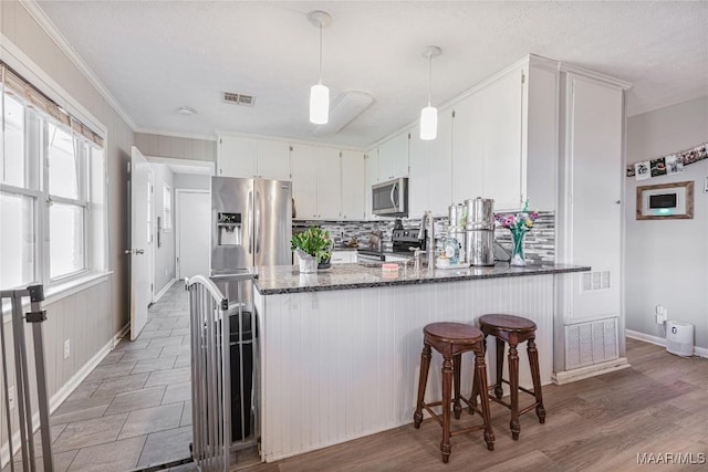 kitchen with appliances with stainless steel finishes, dark stone countertops, white cabinets, decorative backsplash, and kitchen peninsula