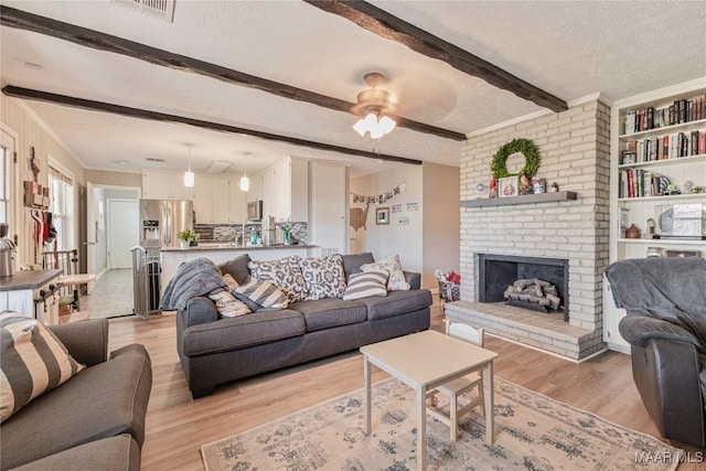 living room with crown molding, a brick fireplace, a textured ceiling, light hardwood / wood-style flooring, and beamed ceiling