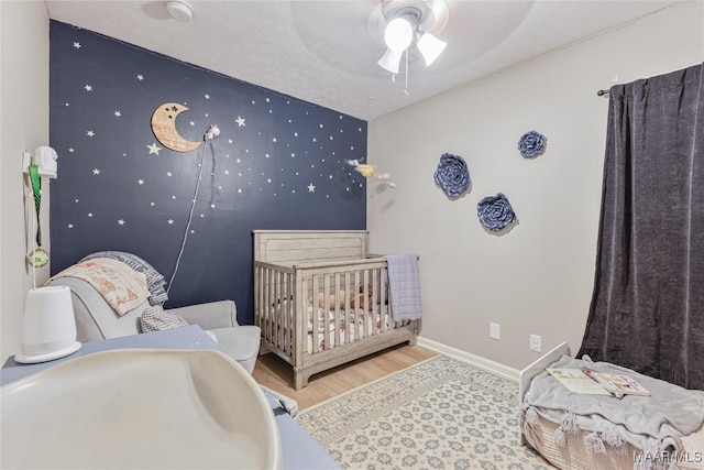 bedroom with a crib, light hardwood / wood-style floors, and ceiling fan