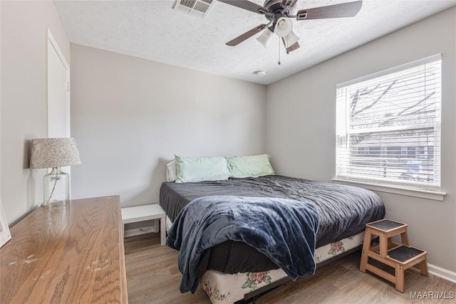 bedroom with ceiling fan, wood-type flooring, and a textured ceiling