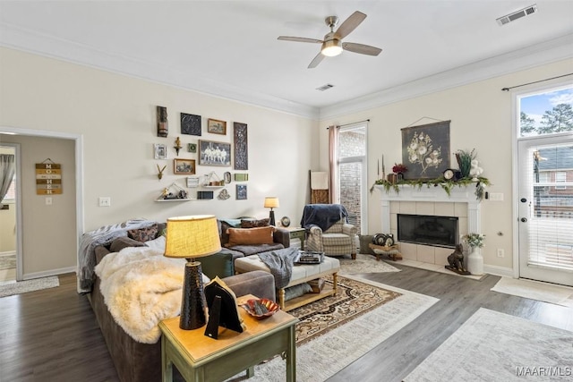 living room featuring a tile fireplace, crown molding, dark hardwood / wood-style floors, and ceiling fan