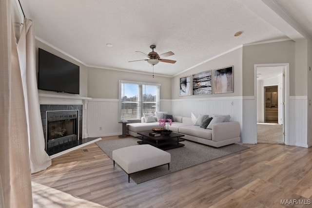 living room featuring lofted ceiling, crown molding, a textured ceiling, a tiled fireplace, and light hardwood / wood-style floors