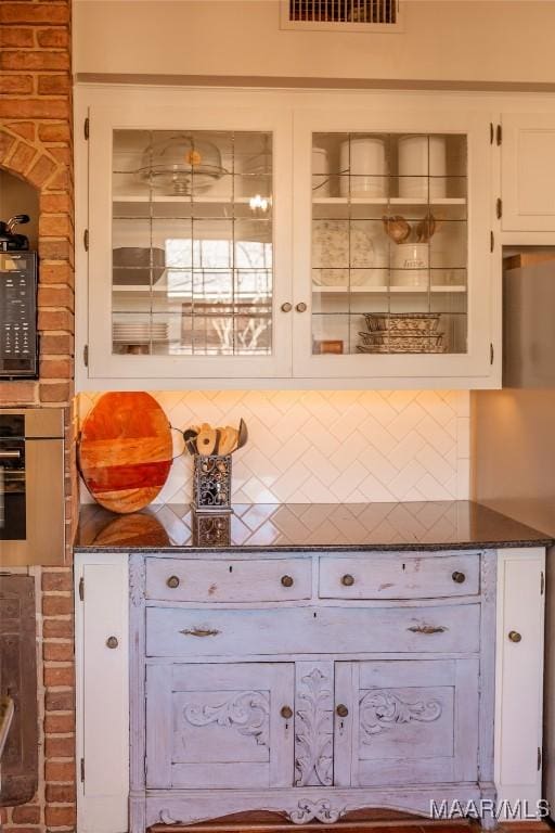 interior space with tasteful backsplash, dark stone counters, and white cabinets