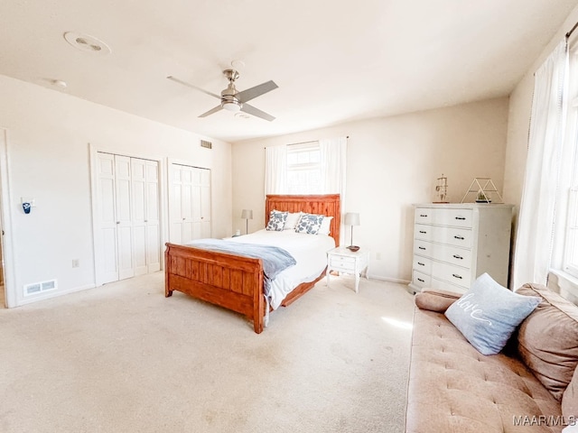 bedroom with multiple windows, two closets, light colored carpet, and ceiling fan