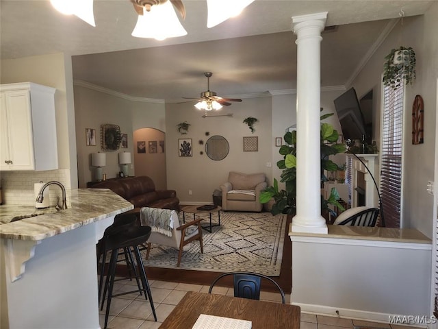 living room with decorative columns, sink, light tile patterned floors, ceiling fan, and crown molding