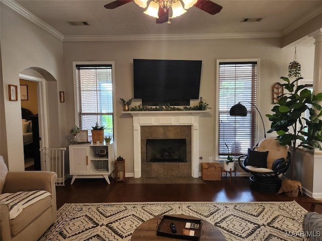 living room featuring ceiling fan, ornamental molding, dark hardwood / wood-style flooring, and a tile fireplace