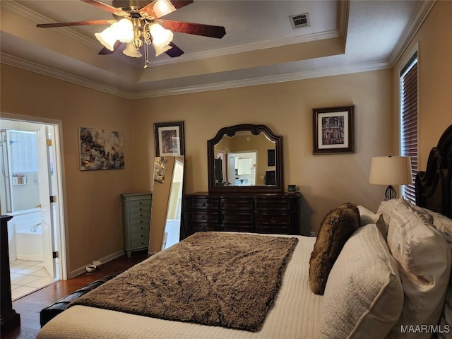 bedroom featuring crown molding, connected bathroom, a tray ceiling, and hardwood / wood-style flooring