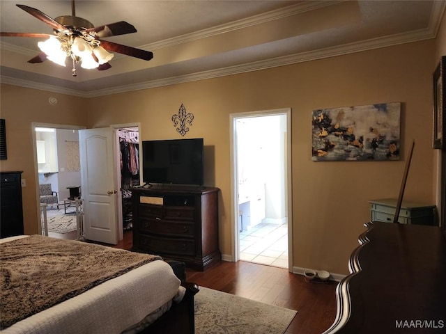 bedroom with crown molding, a walk in closet, dark wood-type flooring, and a tray ceiling