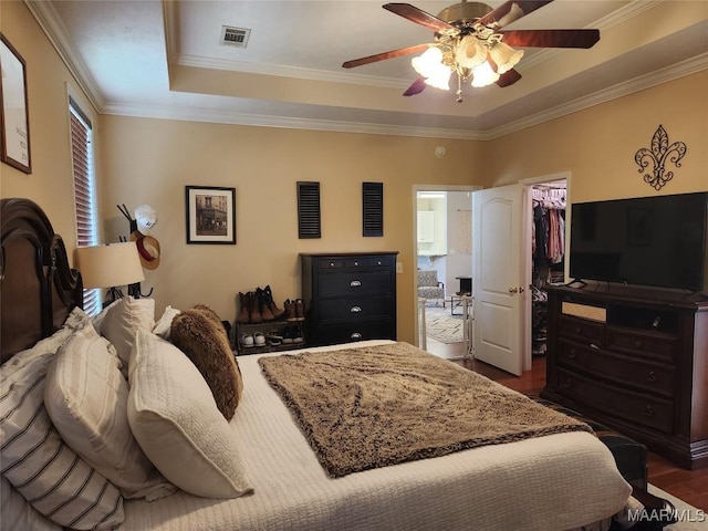 bedroom featuring dark wood-type flooring, a tray ceiling, ornamental molding, a walk in closet, and a closet