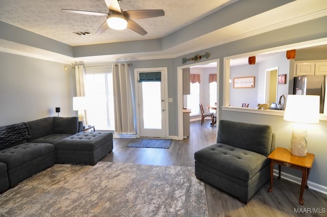 living room featuring a tray ceiling, plenty of natural light, dark hardwood / wood-style floors, and ceiling fan