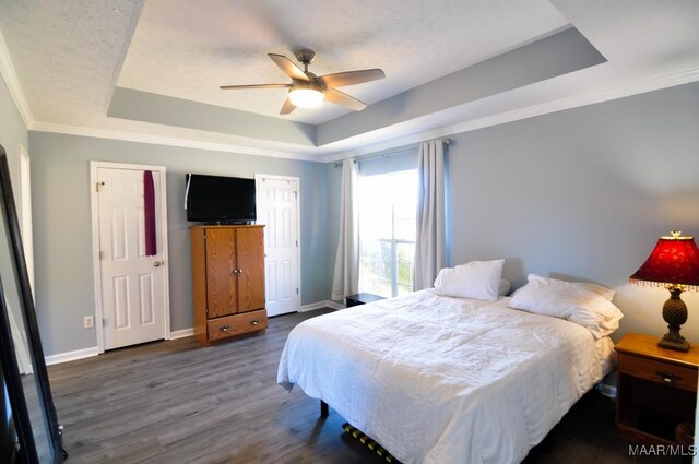 bedroom with dark hardwood / wood-style floors, ceiling fan, a tray ceiling, and crown molding