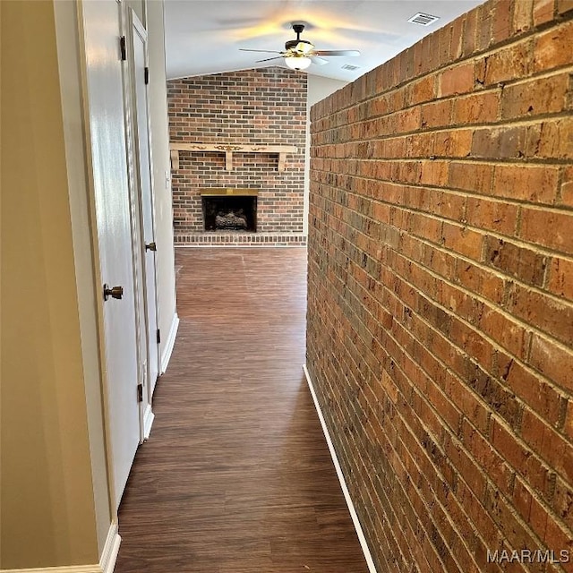 hall featuring dark wood-type flooring, vaulted ceiling, and brick wall