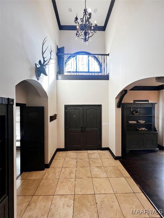 foyer entrance with a high ceiling, ornamental molding, light tile patterned flooring, and a notable chandelier