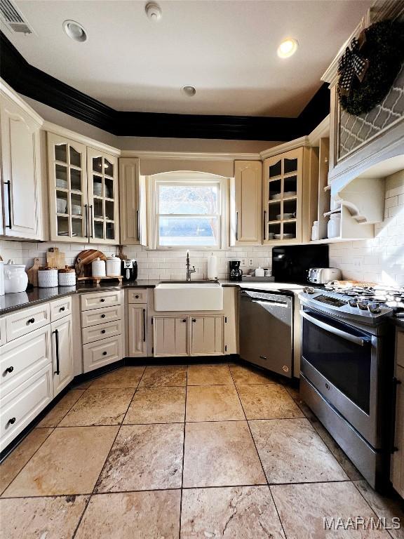 kitchen with tasteful backsplash, appliances with stainless steel finishes, sink, and cream cabinetry